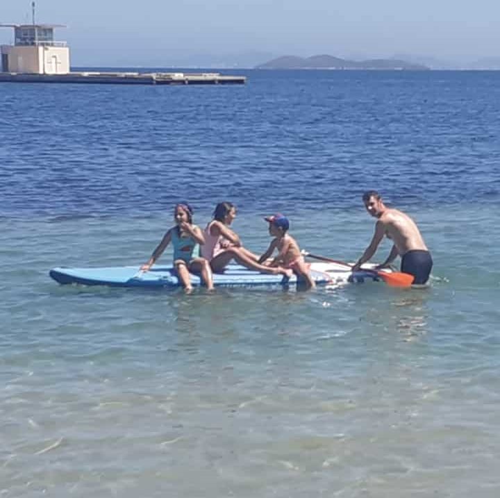 Family enjoy the sea, aided by adult supervision on surf board.